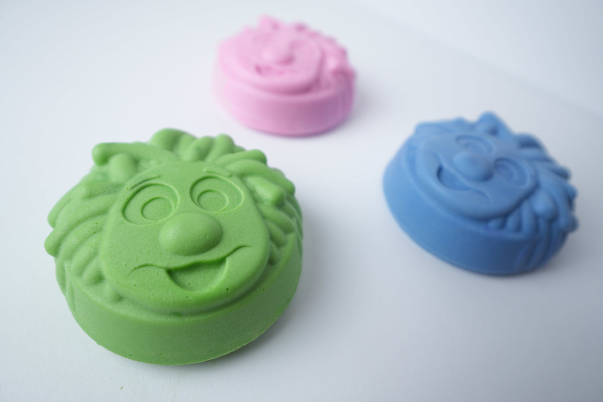 Three Mr. Scrubbadubba soap bars in green, blue, and pink on a white background