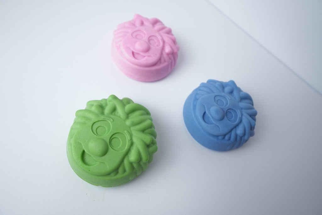 Three Mr. Scrubbadubba soap bars in pink, blue, and green, angled top view