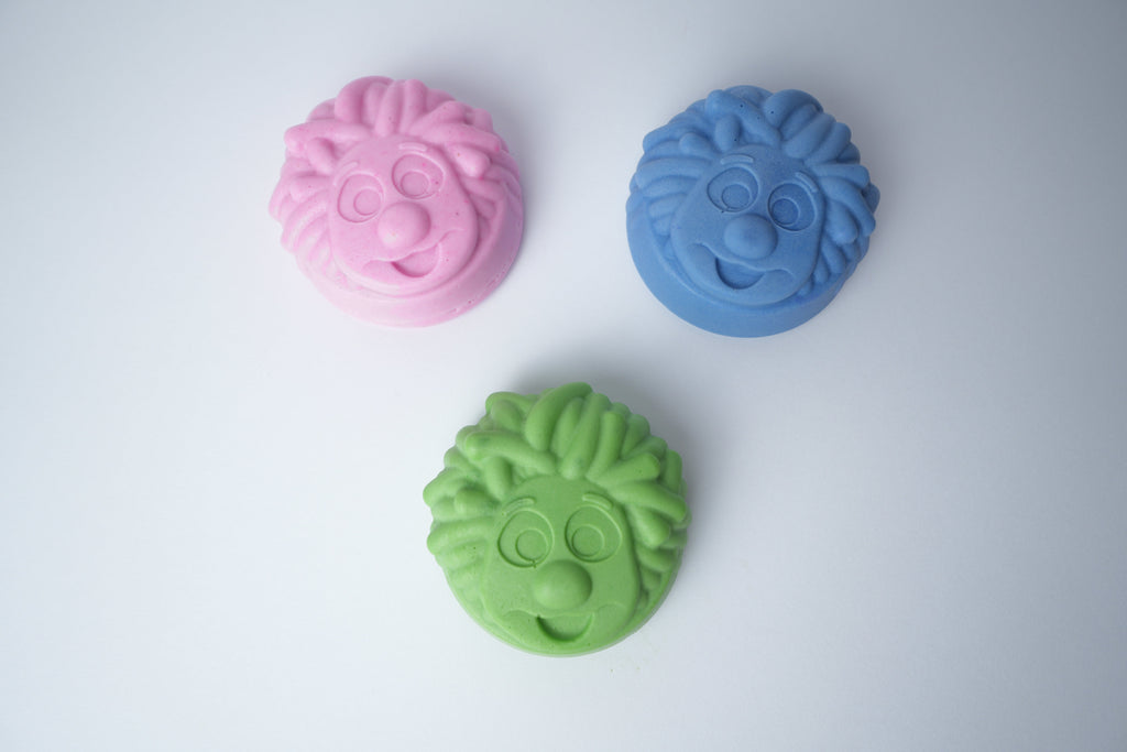 Three Mr. Scrubbadubba soap bars in pink, blue, and green, top view