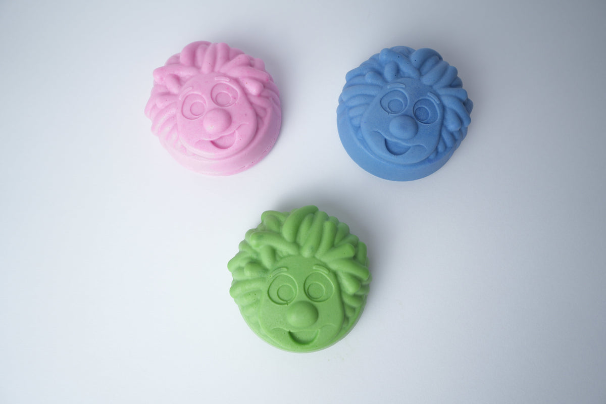 Three Mr. Scrubbadubba soap bars in pink, blue, and green, top view